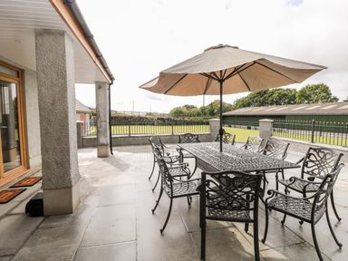 An outdoor patio area with a metal table and eight chairs under a large umbrella at Grooms Quarters at Pant y Gaseg Farm in Ammanford