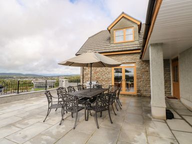 An outdoor patio with a metal dining table and chairs under an umbrella next to a stone house at Grooms Quarters at Pant y Gaseg Farm in Ammanford
