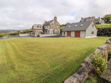 A large yard with green grass and two houses in the background at Grooms Quarters at Pant y Gaseg Farm in Ammanford