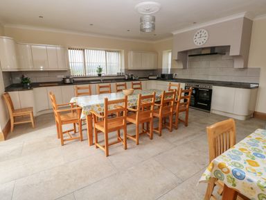 A kitchen with wooden chairs and tables covered with tablecloths a stove and cabinets at Grooms Quarters at Pant y Gaseg Farm in Ammanford