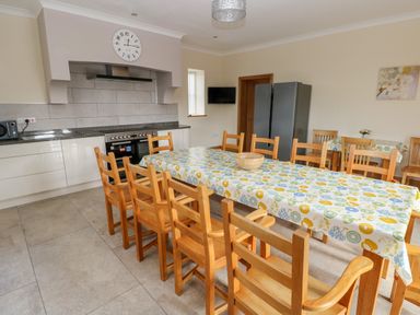 A kitchen with a long dining table covered with a patterned tablecloth and wooden chairs at Grooms Quarters at Pant y Gaseg Farm in Ammanford