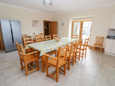 A dining room with a long table covered with a patterned tablecloth surrounded by wooden chairs at Grooms Quarters at Pant y Gaseg Farm in Ammanford