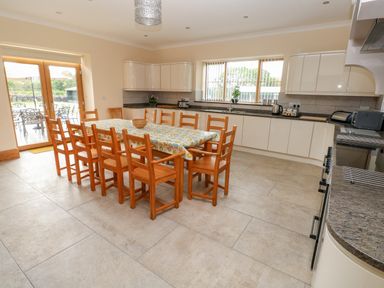 A kitchen with a large dining table and wooden chairs a countertop with appliances and cabinets and patio doors leading outside at Grooms Quarters at Pant y Gaseg Farm in Ammanford