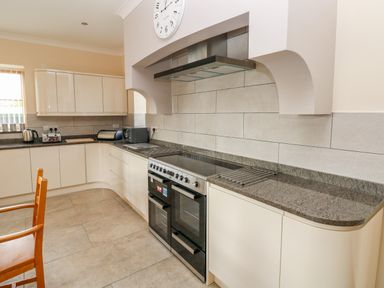 A kitchen with white cabinets a black oven a wooden chair and countertop appliances at Grooms Quarters at Pant y Gaseg Farm in Ammanford
