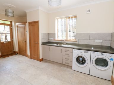 A utility room with a sink, washing machine, dryer, two wooden doors, and a wooden framed external door at Grooms Quarters at Pant y Gaseg Farm in Ammanford