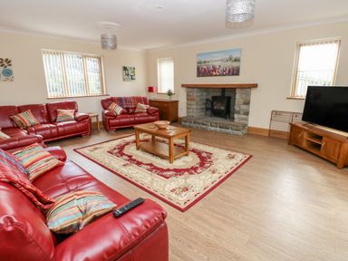 A living room with red leather sofas a wooden coffee table a rug a stone fireplace and a TV at Grooms Quarters at Pant y Gaseg Farm in Ammanford