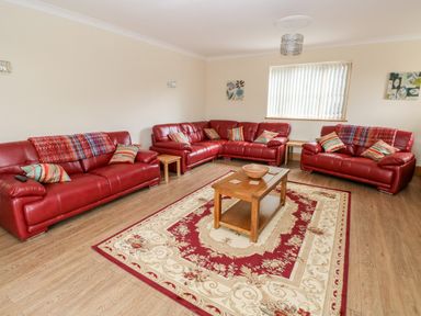 A living room with red leather sofas a wooden coffee table and a patterned rug at Grooms Quarters at Pant y Gaseg Farm in Ammanford