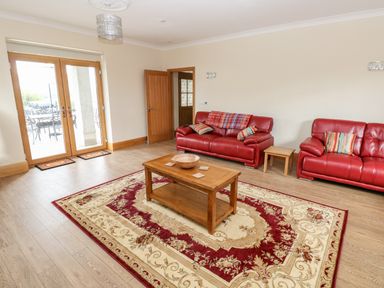A living room with red sofas wooden coffee table and patterned rug at Grooms Quarters at Pant y Gaseg Farm Ammanford