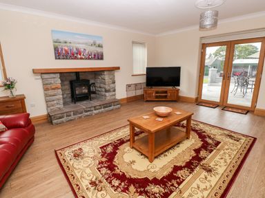 A living room with a stone fireplace wooden coffee table and television with glass doors at Grooms Quarters at Pant y Gaseg Farm in Ammanford