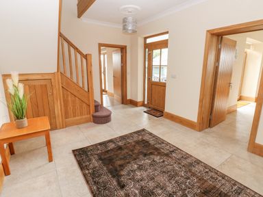 An entrance hallway with a wooden staircase a wooden door a small wooden table with a plant and a large patterned rug on the floor at Grooms Quarters at Pant y Gaseg Farm in Ammanford