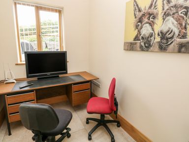 A small office with a desk holding a monitor and remote and two office chairs at Grooms Quarters at Pant y Gaseg Farm in Ammanford