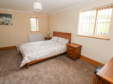 A bedroom with a double bed bedside tables a chair windows and a radiator at Grooms Quarters at Pant y Gaseg Farm Ammanford
