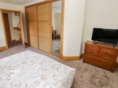 A bedroom with a patterned bedspread a wooden dresser with a TV and a closet with sliding doors at Grooms Quarters at Pant y Gaseg Farm in Ammanford