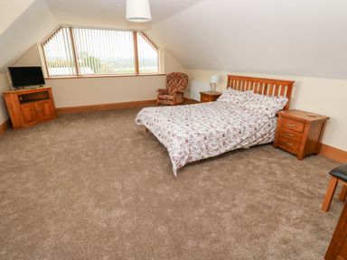 A bedroom with a bed floral bedspread armchair TV on wooden stand and nightstands at Grooms Quarters at Pant y Gaseg Farm in Ammanford
