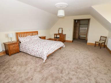 A bedroom with a double bed and floral bedding two bedside tables lamp a dressing table chair and an open closet space at Grooms Quarters at Pant y Gaseg Farm in Ammanford