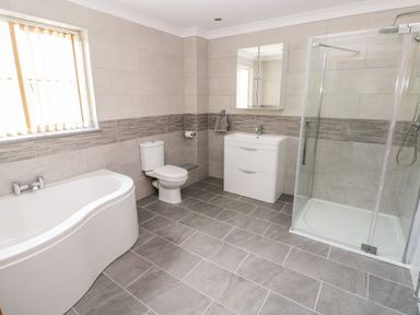 A bathroom with a bathtub toilet sink with mirror and a glass shower enclosure at Grooms Quarters at Pant y Gaseg Farm in Ammanford