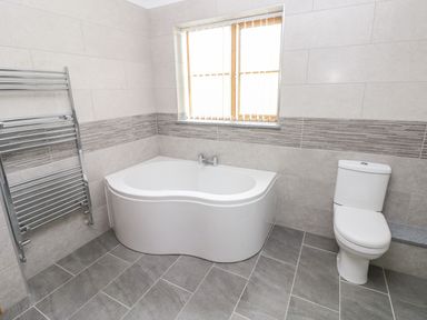A bathroom with a corner bathtub a toilet a towel radiator and a window at Grooms Quarters at Pant y Gaseg Farm in Ammanford