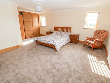 A bedroom with a bed a floral armchair two bedside tables and wooden sliding closet doors at Grooms Quarters at Pant y Gaseg Farm in Ammanford
