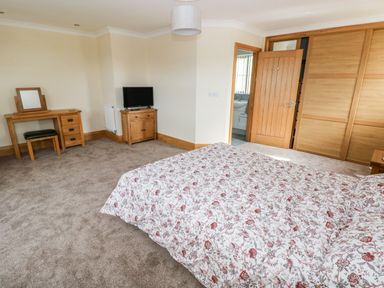 A bedroom with a bed covered in floral bedding a wooden dressing table with mirror a small wooden cabinet with a TV and a wooden door at Grooms Quarters at Pant y Gaseg Farm Ammanford