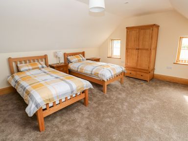 A bedroom with two single beds a wooden wardrobe and two small windows at Grooms Quarters at Pant y Gaseg Farm in Ammanford
