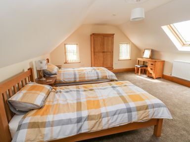 A bedroom with two single beds a wooden wardrobe and a wooden dressing table with a chair at Grooms Quarters at Pant y Gaseg Farm in Ammanford