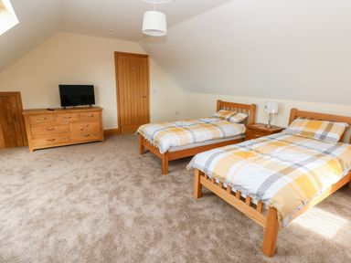 A bedroom with two single beds a wooden dresser with a TV on top and a wooden door at Grooms Quarters at Pant y Gaseg Farm in Ammanford