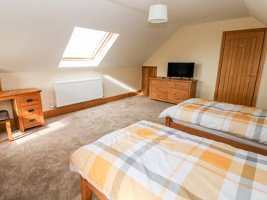 A bedroom with two beds a wooden dresser a desk with a chair a skylight window and a wooden door at Grooms Quarters at Pant y Gaseg Farm in Ammanford
