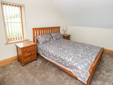 A bedroom with a wooden bed frame and floral bedspread two wooden bedside tables and a window with vertical blinds at Grooms Quarters at Pant y Gaseg Farm Ammanford
