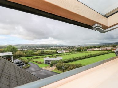 A view of green fields and houses seen through an open roof window at Grooms Quarters at Pant y Gaseg Farm in Ammanford