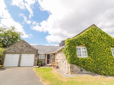 A stone house with two white garage doors and ivy covering part of the wall at Coquet View Cottage in Rothbury