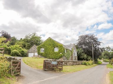 A stone cottage with ivy on the walls and a wooden gate next to a road at Coquet View Cottage in Rothbury