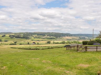 A grassy field with a wooden fence and rolling hills in the background at Coquet View Cottage in Rothbury