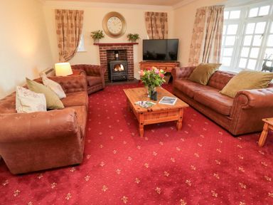 A living room with two brown sofas a brown armchair a wooden coffee table with flowers a fireplace and a television at Coquet View Cottage Rothbury