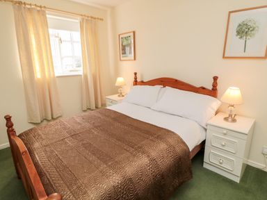 A bedroom with a wooden bed and brown quilt two white bedside tables with lamps and framed pictures on walls at Coquet View Cottage in Rothbury