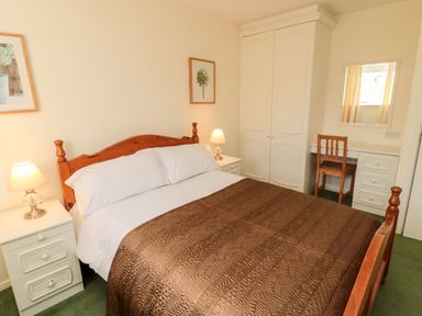 A bedroom with a double bed brown quilt two bedside tables with lamps a wardrobe and a dressing table with a chair at Coquet View Cottage Rothbury