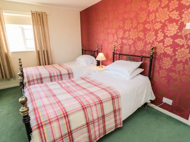 A bedroom with two single beds with plaid blankets a nightstand with a lamp and floral wallpaper at Coquet View Cottage in Rothbury