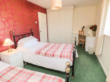 A bedroom with two single beds a white nightstand a wardrobe a dressing table with a chair and a window at Coquet View Cottage in Rothbury