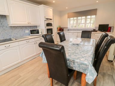 A kitchen with white cabinets a dining table covered with a patterned tablecloth and six black chairs Coquet View Cottage Rothbury