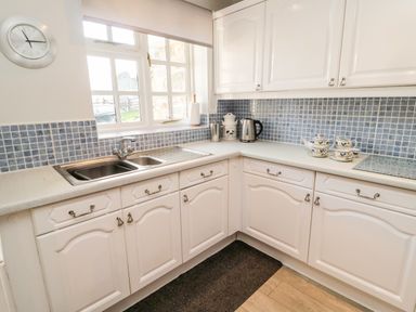 A kitchen with white cabinets blue tiled backsplash stainless steel sink and window at Coquet View Cottage in Rothbury