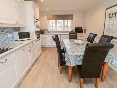 A kitchen with white cabinets a dining table with black chairs and a window with a blind at Coquet View Cottage in Rothbury