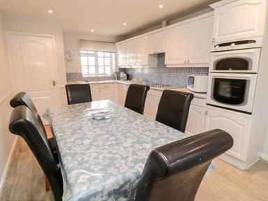 A kitchen with a dining table covered with a floral tablecloth and six dark chairs at Coquet View Cottage in Rothbury