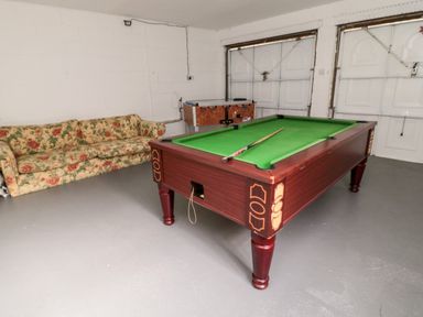 A pool table with a cue stick in a room with a floral patterned sofa and a foosball table at Coquet View Cottage Rothbury