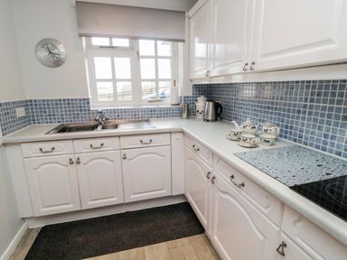 A kitchen with white cabinets blue tiled backsplash a sink under a window and a tea set on the countertop at Coquet View Cottage in Rothbury