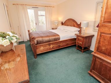 A bedroom with wooden bed frame bedside tables lamps dresser and basket of flowers at Coquet View Cottage in Rothbury