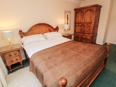 A bedroom with a wooden bed with a brown blanket two bedside tables with lamps and a wooden wardrobe at Coquet View Cottage in Rothbury