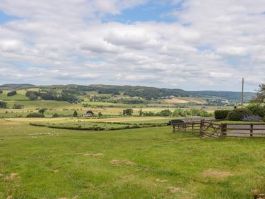 A grassy field with wooden fences and distant hills under a cloudy sky at The Steadings in Rothbury