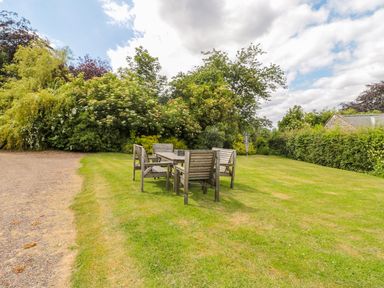A garden with a wooden table and benches on grass with trees and bushes at The Steadings in Rothbury