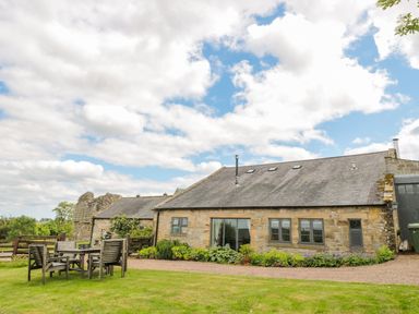 A stone cottage with garden furniture on a lawn outside at The Steadings in Rothbury