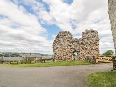 A stone wall ruin next to a wooden gate on a rural road with houses and hills in the background at The Steadings in Rothbury