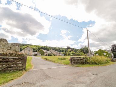 A rural stone building complex with wooden gates and a driveway leading to houses at The Steadings in Rothbury